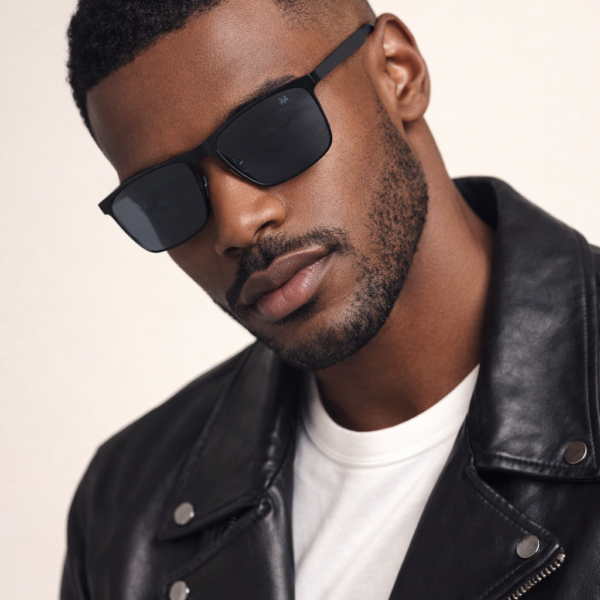 Portrait of a man with short curly hair wearing black sunglasses and a black leather jacket over a white T-shirt.