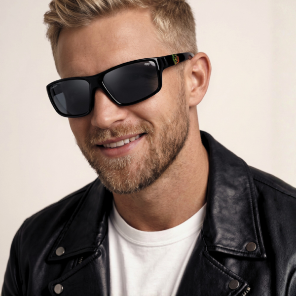 Man with blonde hair wearing black sunglasses and a black leather jacket, smiling at the camera.