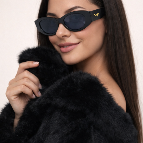 Woman wearing a plush black fur coat and sleek black sunglasses with a small gold 'VV' logo on the temple, posing against a light background.