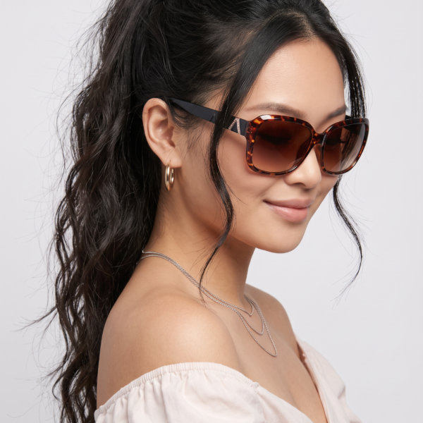 Close-up portrait of a woman wearing tortoiseshell oversized sunglasses, with a high ponytail, gold hoop earrings, and a white off-the-shoulder top.