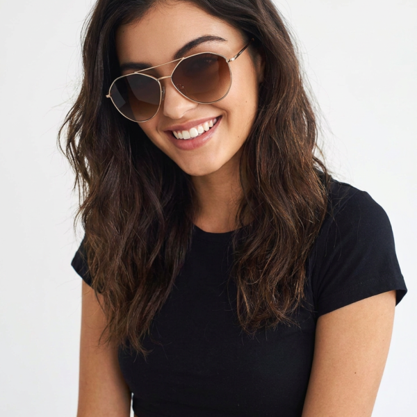 Smiling woman wearing round sunglasses and a black crop top against a light background.