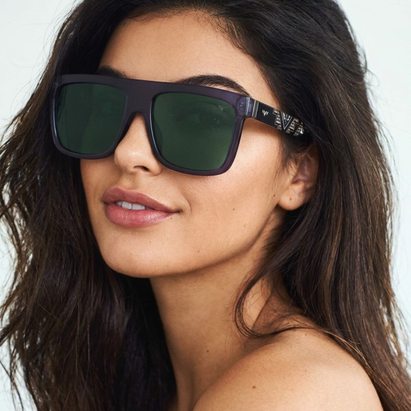 Close-up of a woman with long dark hair wearing oversized black sunglasses, facing slightly left.