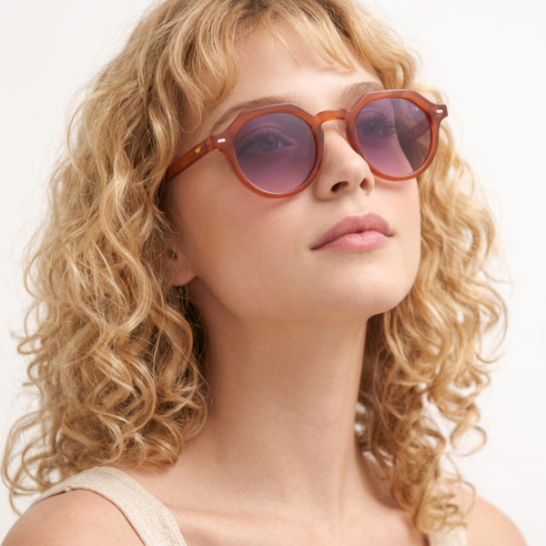 Portrait of a woman with blonde curly hair wearing orange round sunglasses, looking upward.