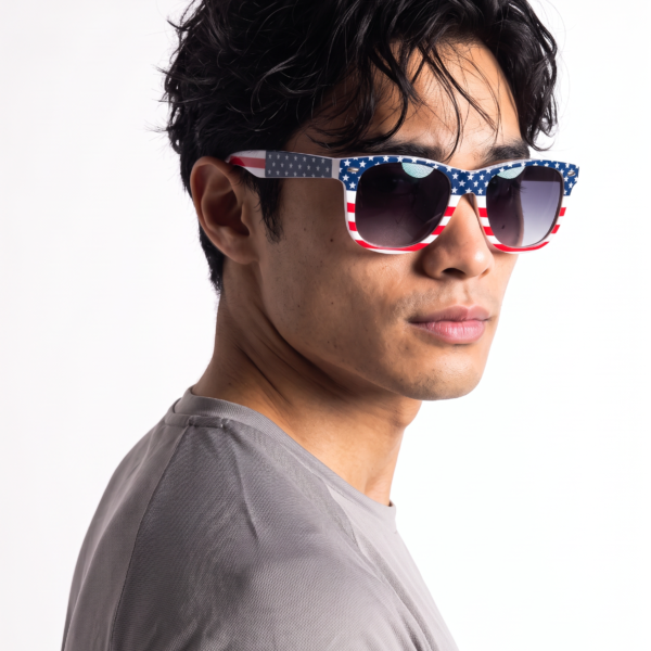 Profile of a young man wearing red-white-blue star-pattern sunglasses against a white background, gray T-shirt visible at the shoulder