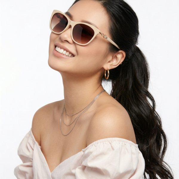 Smiling woman with beige sunglasses, off-shoulder light pink top, layered silver necklaces and gold hoop earrings.
