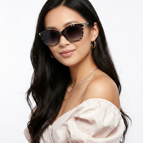 Woman with long dark hair wearing oversized sunglasses, an off-the-shoulder pink top, and layered necklaces.