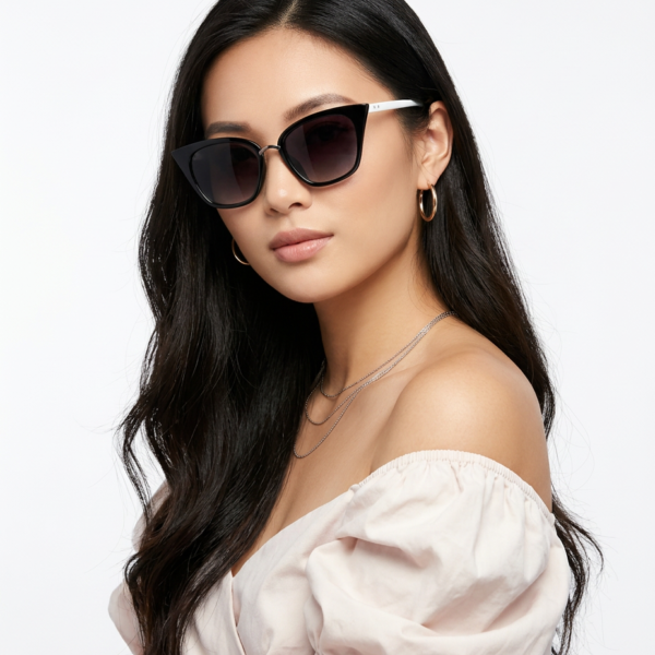 Woman wearing oversized black cat-eye sunglasses with white temples, off-the-shoulder blouse, and layered necklaces.