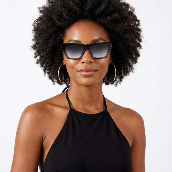 Woman with natural curly hair wearing oversized sunglasses, hoop earrings, and a black halter top, posing against a light background.