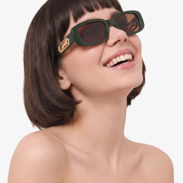 Woman smiling while wearing oversized dark green sunglasses with a gold emblem on the arm and an off-the-shoulder white top