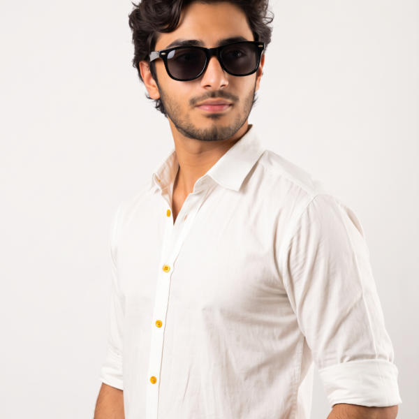 Man with dark hair and beard wearing black sunglasses and a white button-down shirt, posed against a plain light background.
