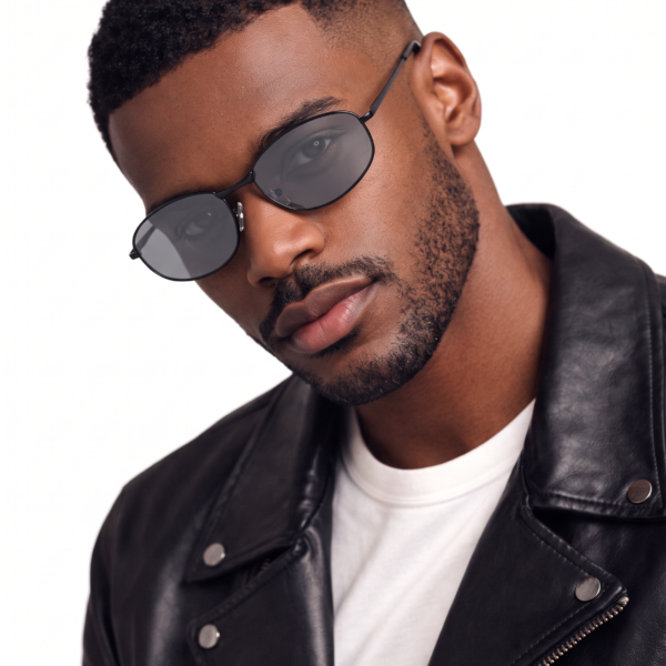 Man wearing black sunglasses and a black leather jacket, head tilted to the side against a white background