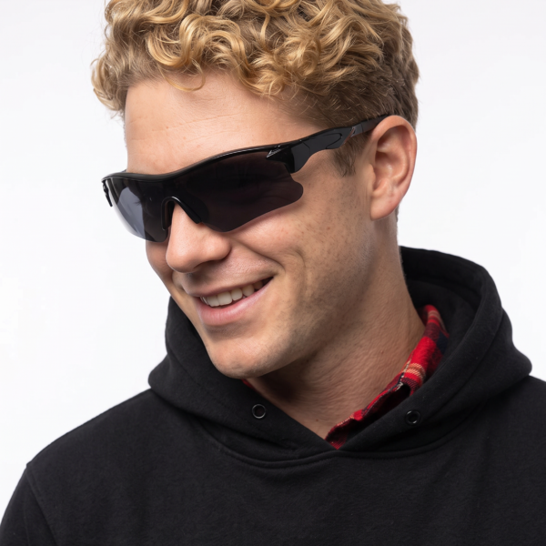 Close-up of a person with curly blond hair wearing black wraparound sunglasses and a black hoodie, smiling slightly.